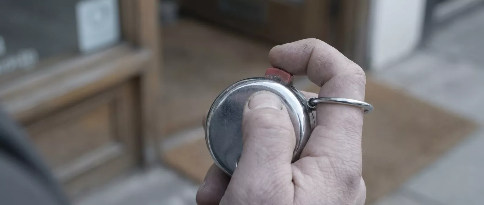 Eine Hand hält am Eingang eines Ladens einen mechanischen Handzähler mit rotem Knopf.